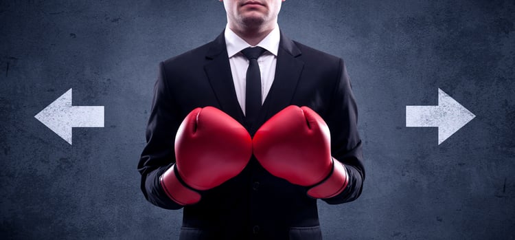 A confident businessman standing with red boxing gloves on his hand in front of arrows pointing in different directions on urban wall background concept.