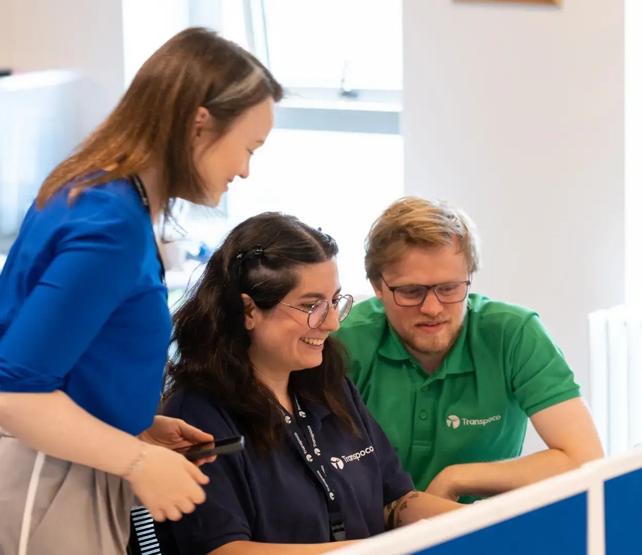 Three smiling Transpoco employees crowding around a desk