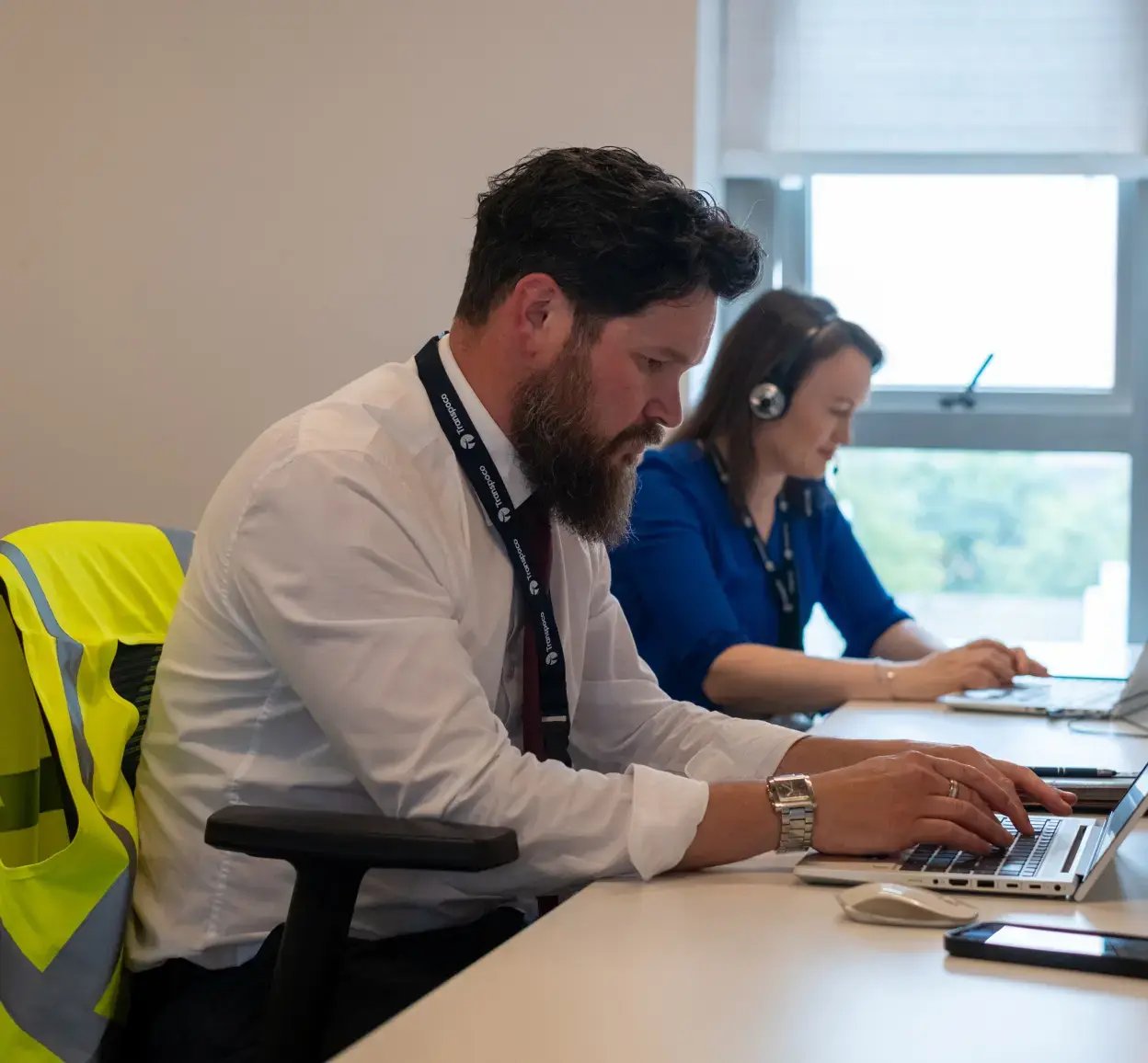 Two Transpoco employees sitting side-by-side at their desks, typing on their laptops