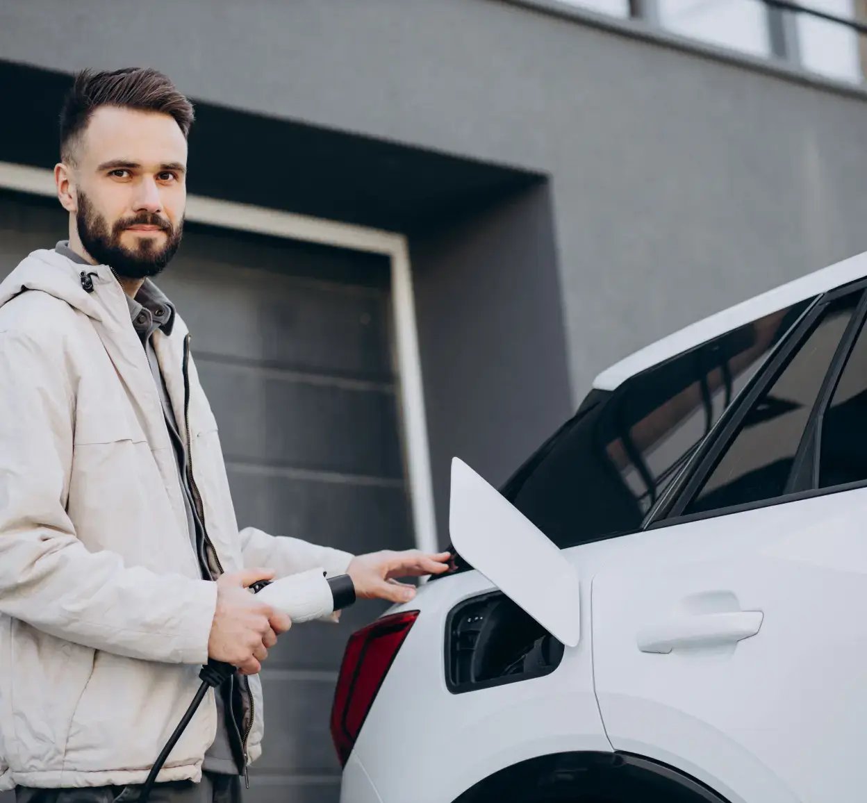 Man in a light grey jacket connecting an electric car to a power socket