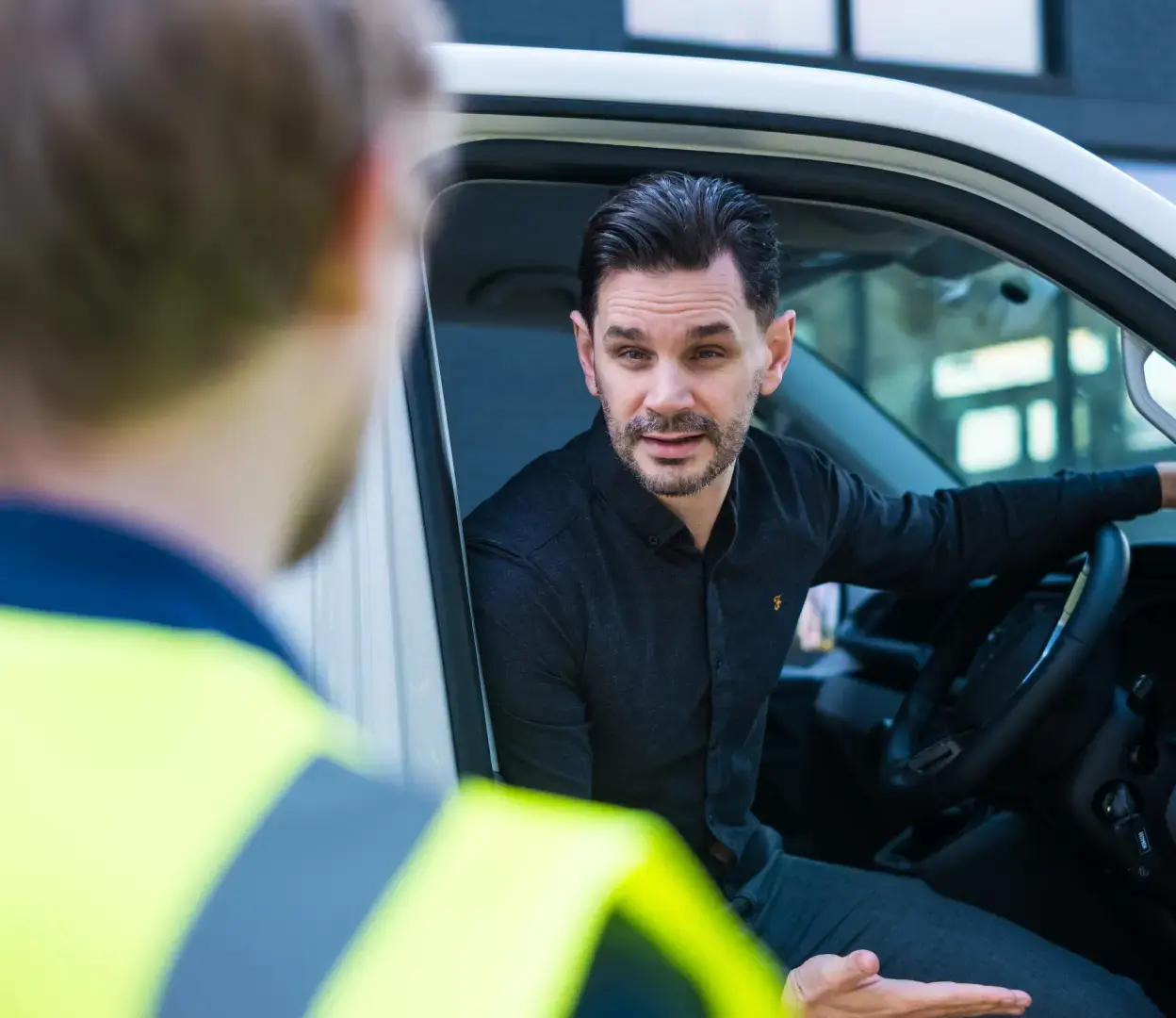 Driver in a black shirt talking to a Transpoco employee from the driver's seat of his van