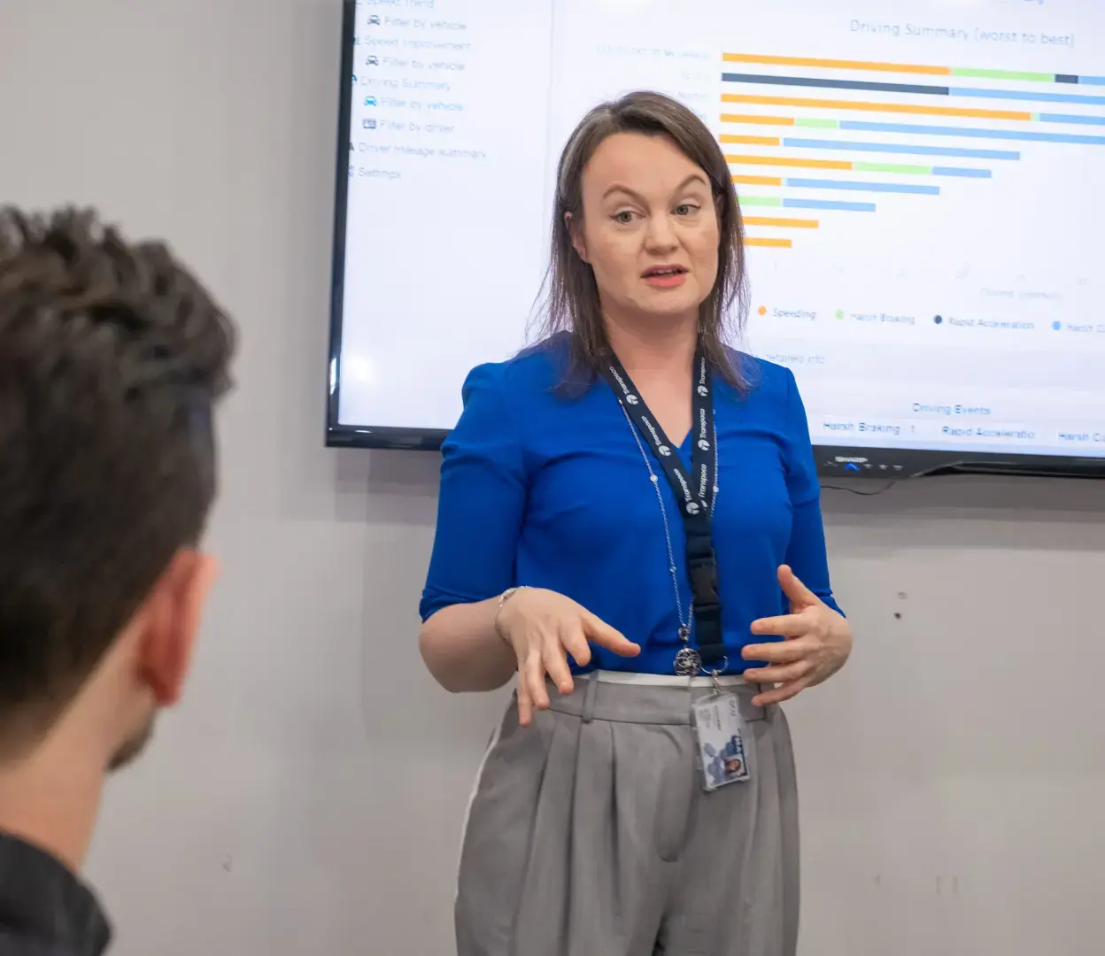 Transpoco employee in blue shirt and grey trousers giving a presentation in front of a TV display